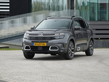 Een grijze Citroën C5 Aircross SUV geparkeerd voor de gevel van een modern gebouw.