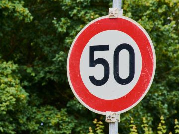 Een snelheidsbouwde kom-verkeersbord met een snelheid van 50 km/u met een groene gebladerteachtergrond.