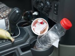 Een proefrit auto-interieur met kattenbakvulling waaronder een bananenschil, een koffiekopje en een waterflesje in de bekerhouders.