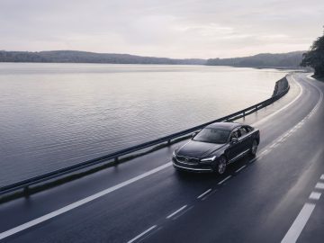 Een Volvo 180 die op een kustweg naast een kalm water rijdt.