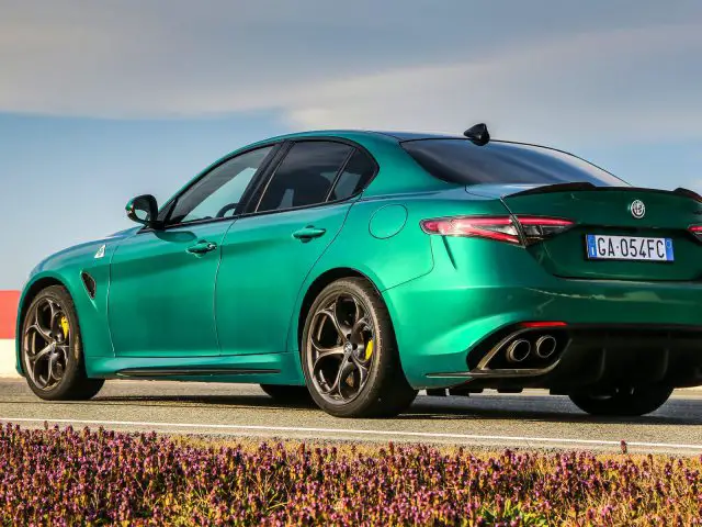 Een groene Alfa Romeo Giulia Quadrifoglio geparkeerd langs de weg met een heldere hemel op de achtergrond.