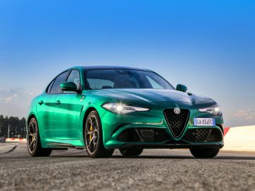 Groene Alfa Romeo Giulia Quadrifoglio op een racecircuit met een helderblauwe lucht op de achtergrond.