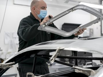 Werknemer met een beschermend masker onderzoekt een Aston Martin DB5 Goldfinger Continuation-auto-onderdeel in een productieomgeving.