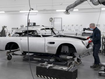 Een technicus werkt aan de carrosserie van een klassieke Aston Martin DB5 Goldfinger Vervolg in een moderne autorestauratiewerkplaats.