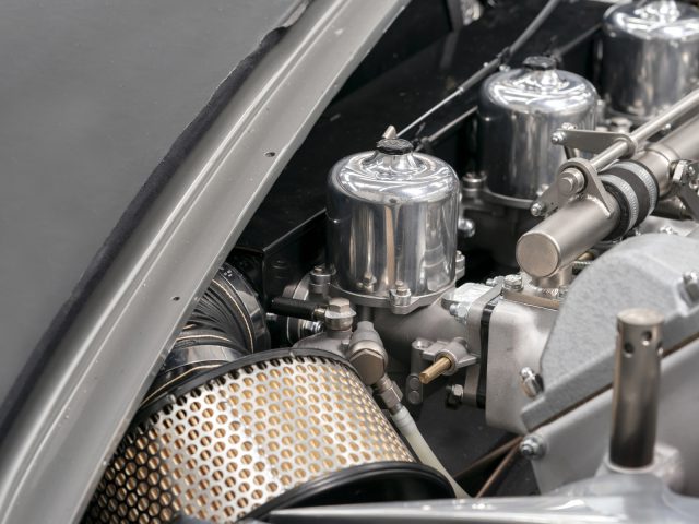 Close-up van een Aston Martin DB5 Goldfinger Continuation-motor met mechanische componenten en een luchtfilter.