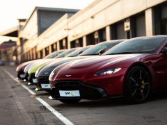 Een rij Aston Martin-sportwagens, begeleid door Tobias Moers, geparkeerd bij een race-pitlane tijdens zonsondergang.