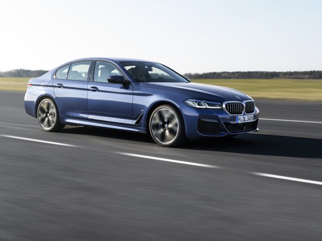 Blauwe BMW 5 Serie sedan in beweging op een gladde weg.