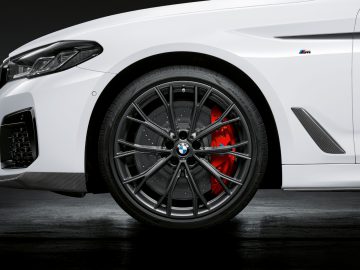 Zijaanzicht van een witte BMW 5 Serie-auto, waarbij het voorwiel en de remklauw worden benadrukt.