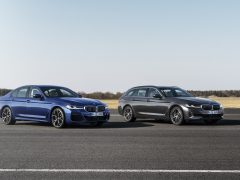Twee auto's uit de BMW 5 Serie staan naast elkaar geparkeerd op een landingsbaan, de ene een sedan en de andere een wagon, in een heldere, zonnige omgeving.