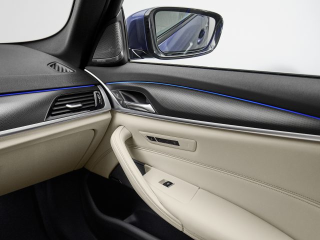 Modern BMW 5 Serie auto-interieur met de focus op het deurpaneel, voorzien van een lederen armsteun, bekleding met blauwe sfeerverlichting en bedieningsschakelaars.