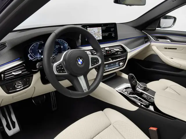 Binnenaanzicht van een modern BMW 5 Serie-voertuig met een leren stuur, digitaal dashboard en infotainmentsysteem.