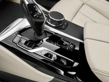 Binnenaanzicht van de middenconsole van een BMW 6 Serie Gran Turismo met automatische versnellingspook, rijmoduskeuzeschakelaar en voertuigbedieningsknoppen met crèmekleurige lederen bekleding.