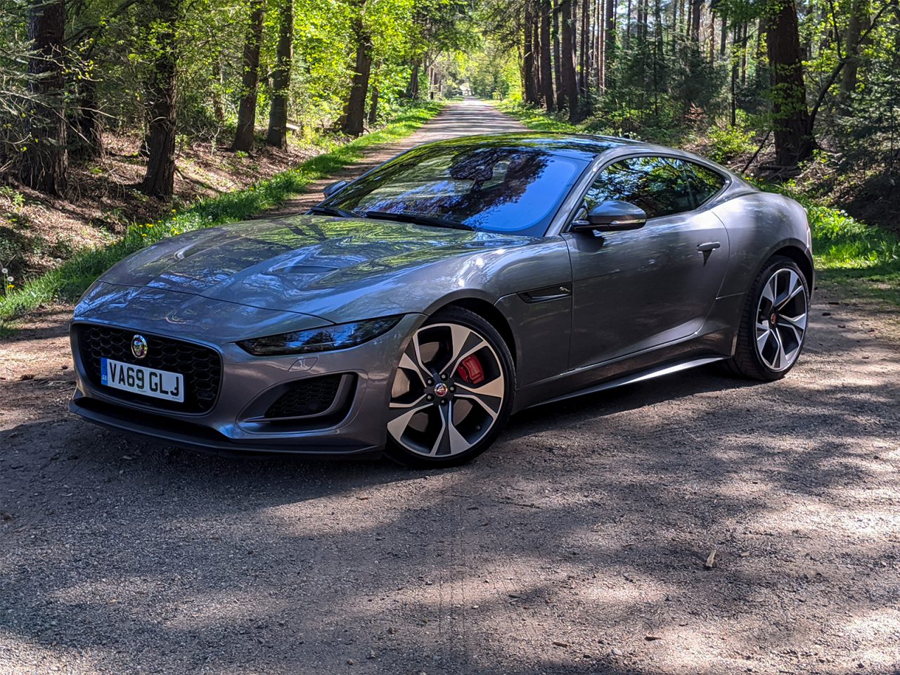 Een grijze Jaguar F-Type geparkeerd op een onverharde weg omgeven door een bos.