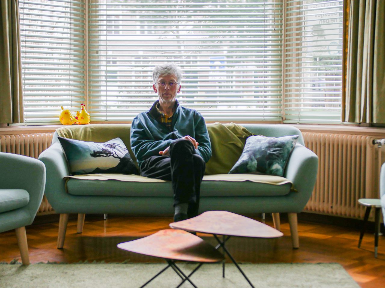 Een persoon die op een bank zit in een goed verlichte kamer met grote ramen en blinden, en leest over stikstof.