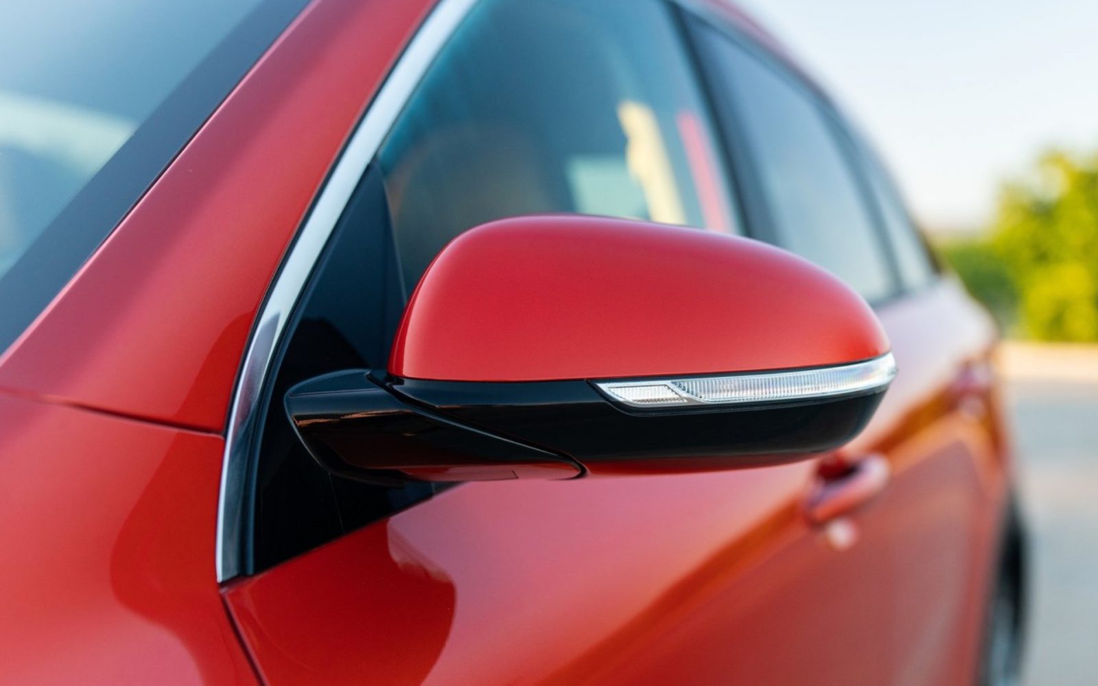 Close-up van de zijspiegel van een rode auto met geïntegreerde richtingaanwijzer, perfect voor autoverkoop.