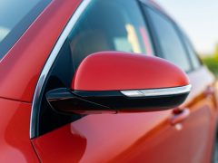 Close-up van de zijspiegel van een rode auto met geïntegreerde richtingaanwijzer, perfect voor autoverkoop.