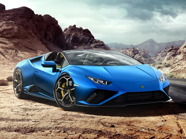 Blauwe Lamborghini Huracán EVO RWD Spyder geparkeerd op een woestijnweg met rotsachtig terrein op de achtergrond.