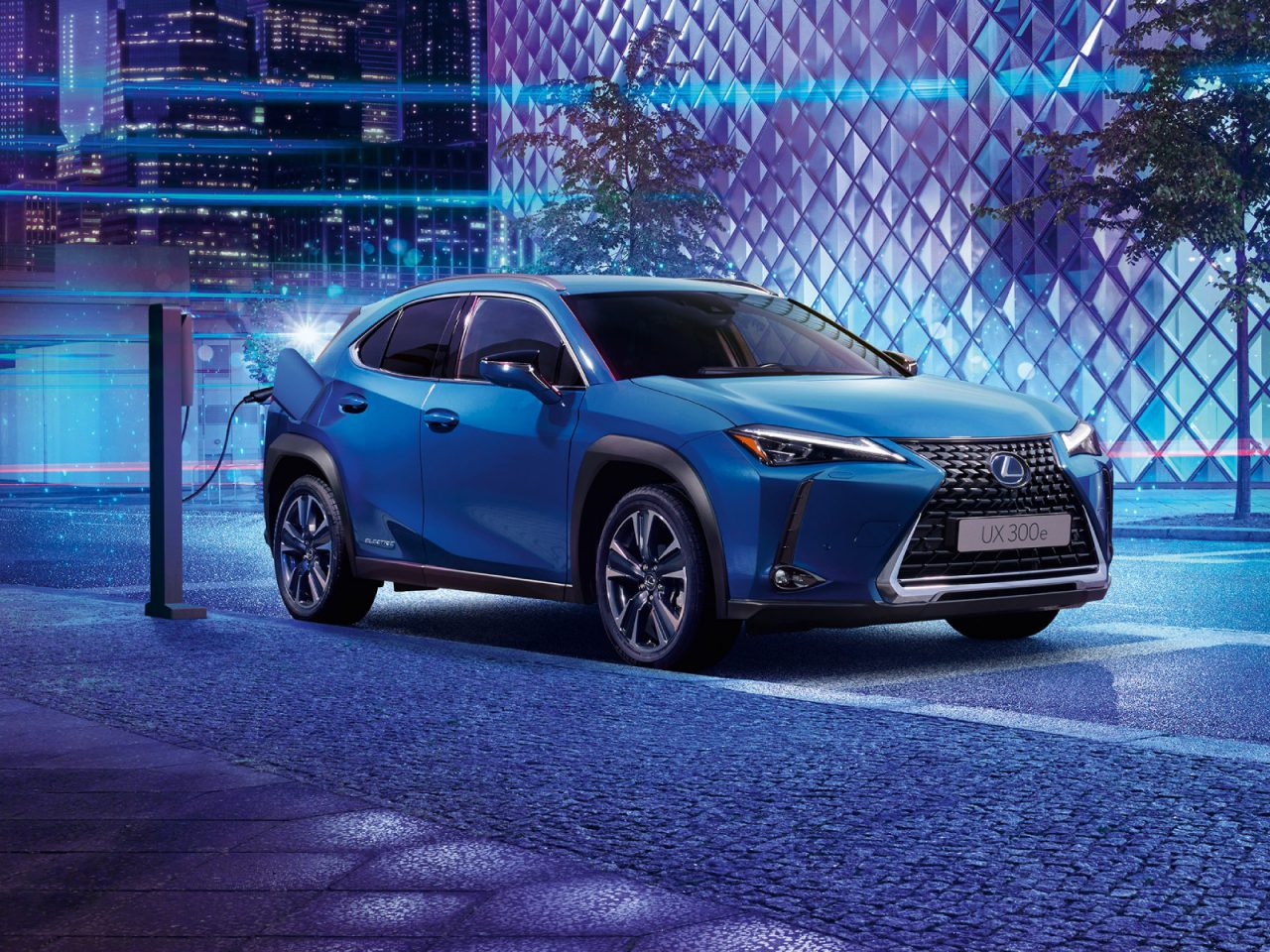 Een Lexus UX Electric opladen bij een station 's nachts in een stedelijke omgeving.