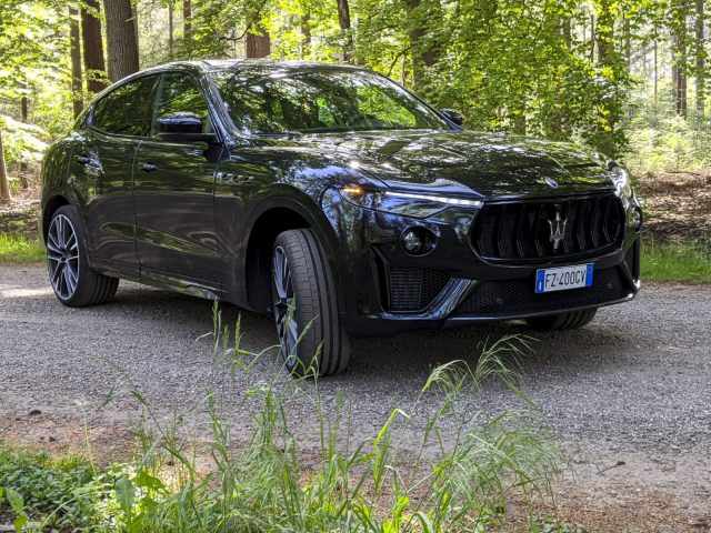 Een zwarte Maserati Levante Trofeo SUV geparkeerd op een grindpad omgeven door bomen.