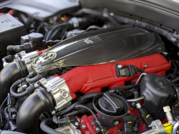 Close-up van een Maserati Levante Trofeo-motorruimte met een rood motorblok en een kap van koolstofvezel.
