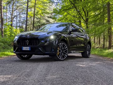 Een zwarte Maserati Levante Trofeo SUV geparkeerd op een bosweg op een zonnige dag.