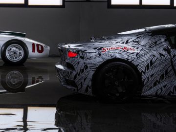 Twee Maserati MC20-sportwagens in een showroom: één met een camouflagefolie en de tekst "Stirling Moss", en een andere met een klassiek wit en rood ontwerp, nummer 10.