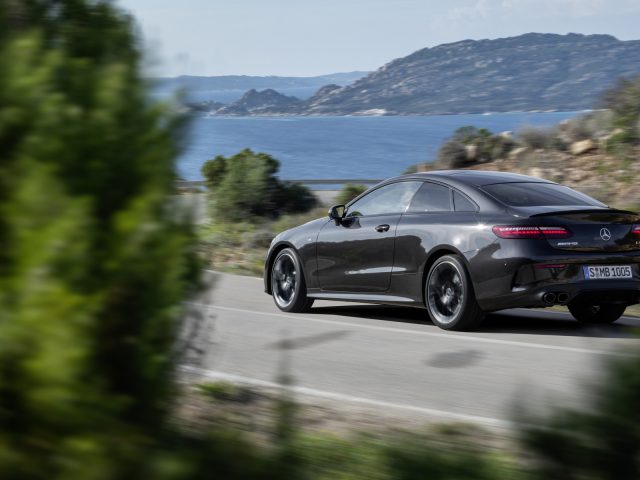 Een luxe coupé van Mercedes-Benz E-Klasse die langs een kustweg rijdt met de oceaan op de achtergrond.