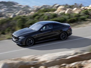 Een zwarte luxe coupé van Mercedes-Benz E-Klasse die op een kustweg rijdt.