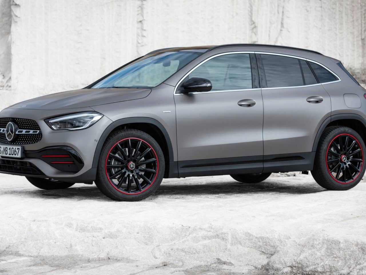 Een moderne grijze Mercedes-Benz SUV met wielen met rode accenten, geparkeerd voor een witte stenen achtergrond.