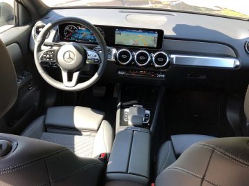 Binnenaanzicht van een moderne Mercedes-Benz GLB met een Mercedes-Benz-logo op het stuur, met het dashboard, het touchscreen-infotainmentsysteem en zwartleren stoelen.