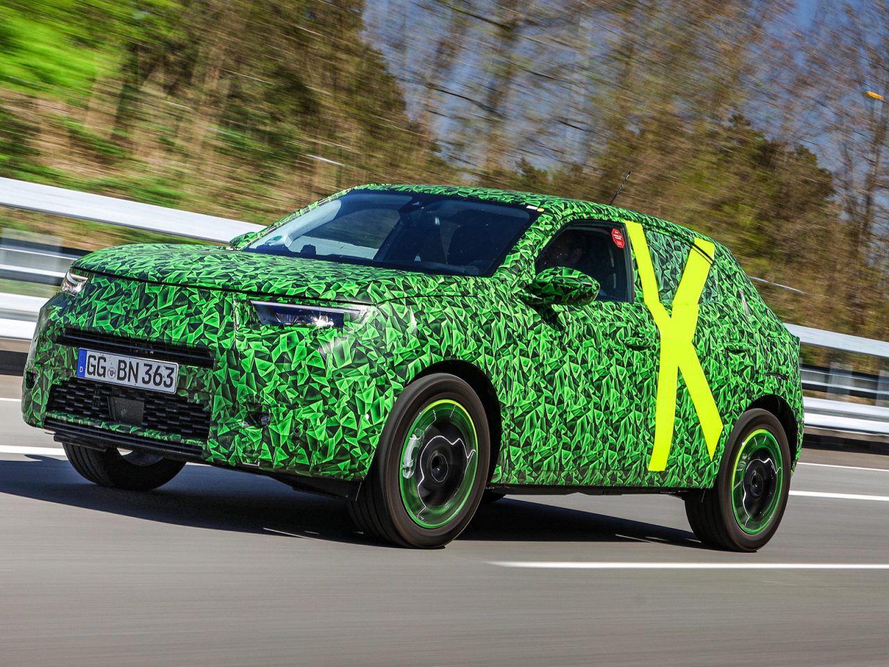 Een in camouflage gewikkeld Opel Mokka-prototype dat tests op de weg ondergaat met een grote gele "x" op de zijkant.