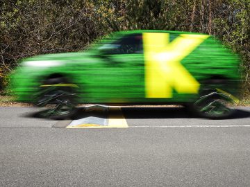 Een groene Opel Mokka SUV in beweging, vastgelegd met een snelheidsonscherpte-effect op een weg met bomen op de achtergrond.