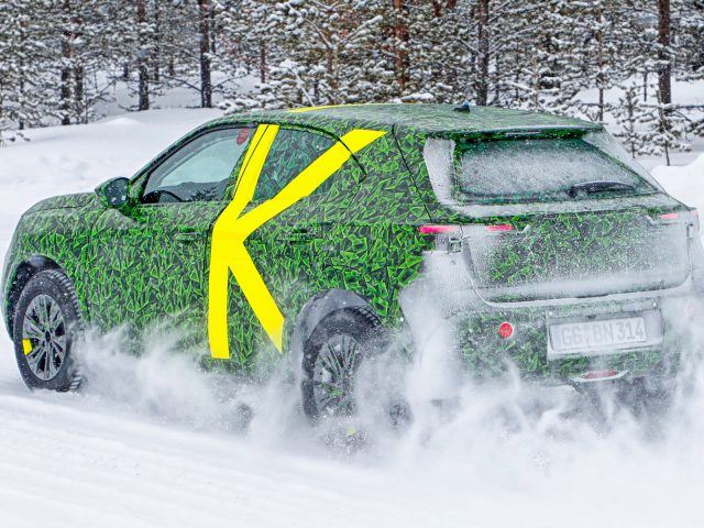 Een gecamoufleerde Opel Mokka-auto die wintertests ondergaat op een besneeuwde weg.