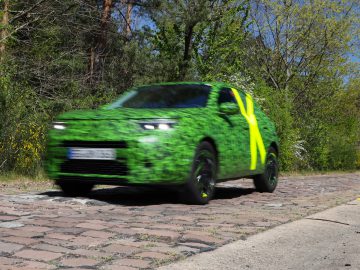 Een Opel Mokka in camouflagepak voert snelheidstests uit op een geplaveide weg, waarbij bewegingsonscherpte beweging illustreert.