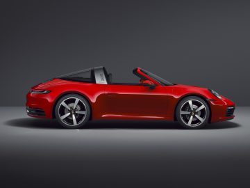 Een rode Porsche 911 Targa converteerbare sportwagen tegen een grijze achtergrond.