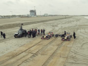 Een filmploeg en cast verzamelden zich op een strand met apparatuur voor een "Dutch Road Trip" kartbaanopstelling.
