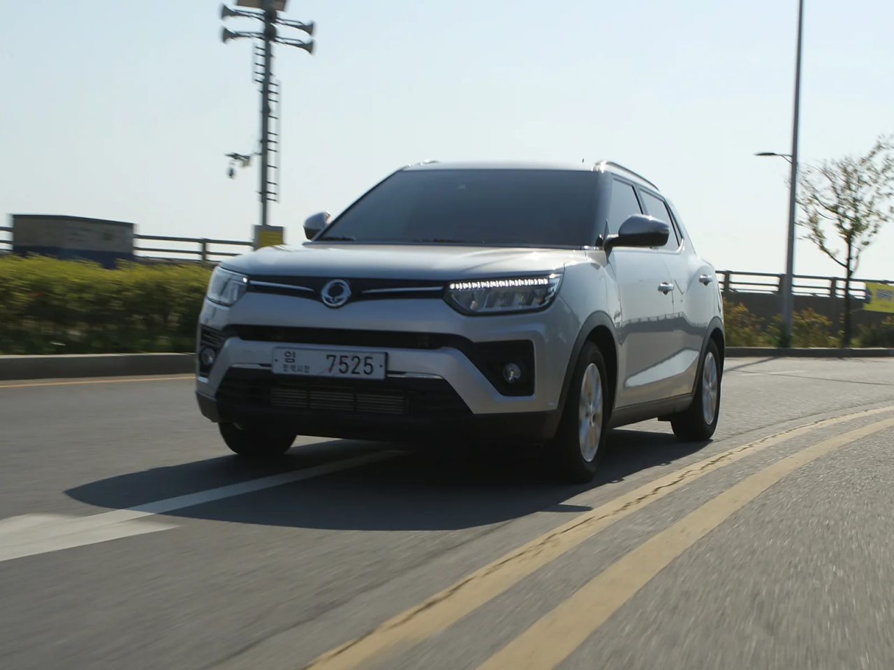 SsangYong Tivoli rijdt op een zonnige dag op een open weg met heldere hemel.