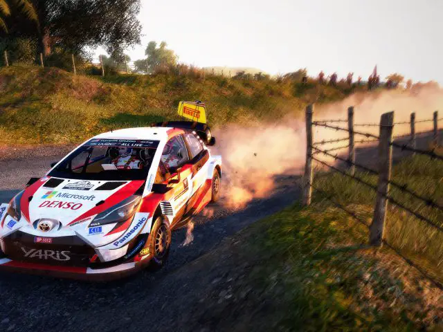 Een WRC 9-gameplay-rallyautorace op een onverharde weg, waarbij stof opwaait bij zonsondergang.