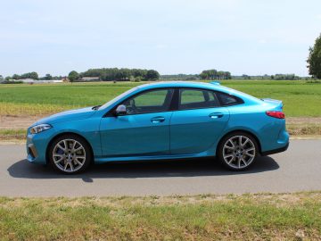 Helderblauwe BMW 2 Serie Gran Coupé geparkeerd aan de kant van een weg met velden op de achtergrond.
