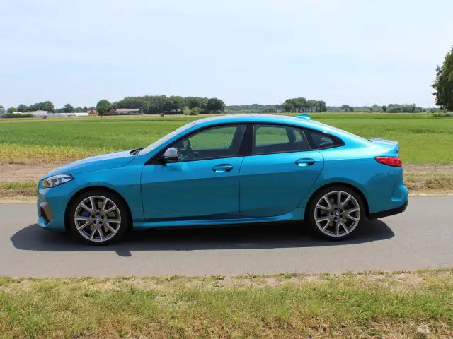 Helderblauwe BMW 2 Serie Gran Coupé geparkeerd aan de kant van een weg met velden op de achtergrond.