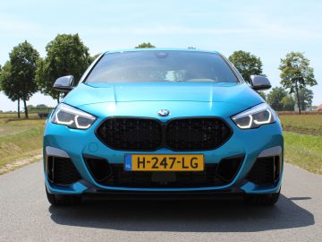 Een blauwe BMW 2 Serie Gran Coupé geparkeerd op een asfaltweg met een landelijk landschap op de achtergrond.