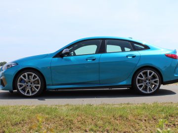 Een blauwe BMW 2 Serie Gran Coupé geparkeerd aan de kant van een weg met een heldere hemel op de achtergrond.