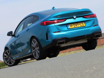 Blauwe BMW 2 Serie Gran Coupé geparkeerd op een asfaltoppervlak met een heldere hemel op de achtergrond.