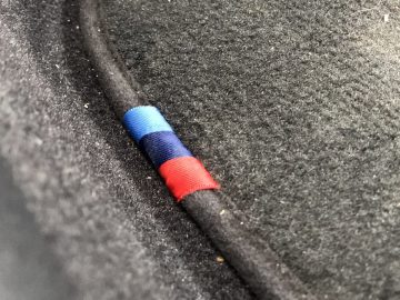 Een rode en blauwe stoffen kabel verborgen in de groef van een zwart gestructureerd oppervlak van de BMW 2 Serie Gran Coupé.