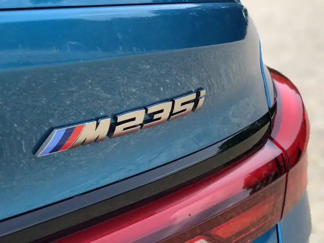 Close-up van een BMW 2 Serie Gran Coupé-autobadge met een met stof bedekte kofferbak.