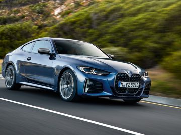 Een blauwe BMW 4 Serie Coupé snelt over een snelweg met een natuurlijk landschap op de achtergrond.