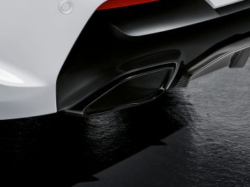Close-up van de achterbumper en uitlaatpijp van een BMW 4 Serie Coupé met een donkere achtergrond.