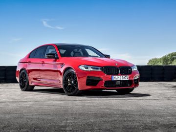 BMW M5 sedan geparkeerd op asfalt met een heldere hemelachtergrond.