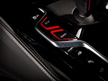 Close-up van de sportmodusknop en de rijmoduskeuzeschakelaar van een BMW M5 op een zwarte console.