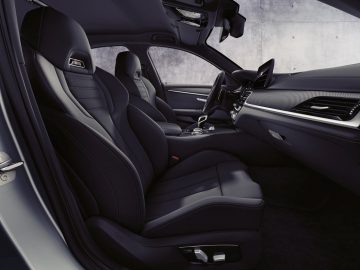 Binnenaanzicht van een moderne BMW M5 met leren stoelen en een middenconsole.